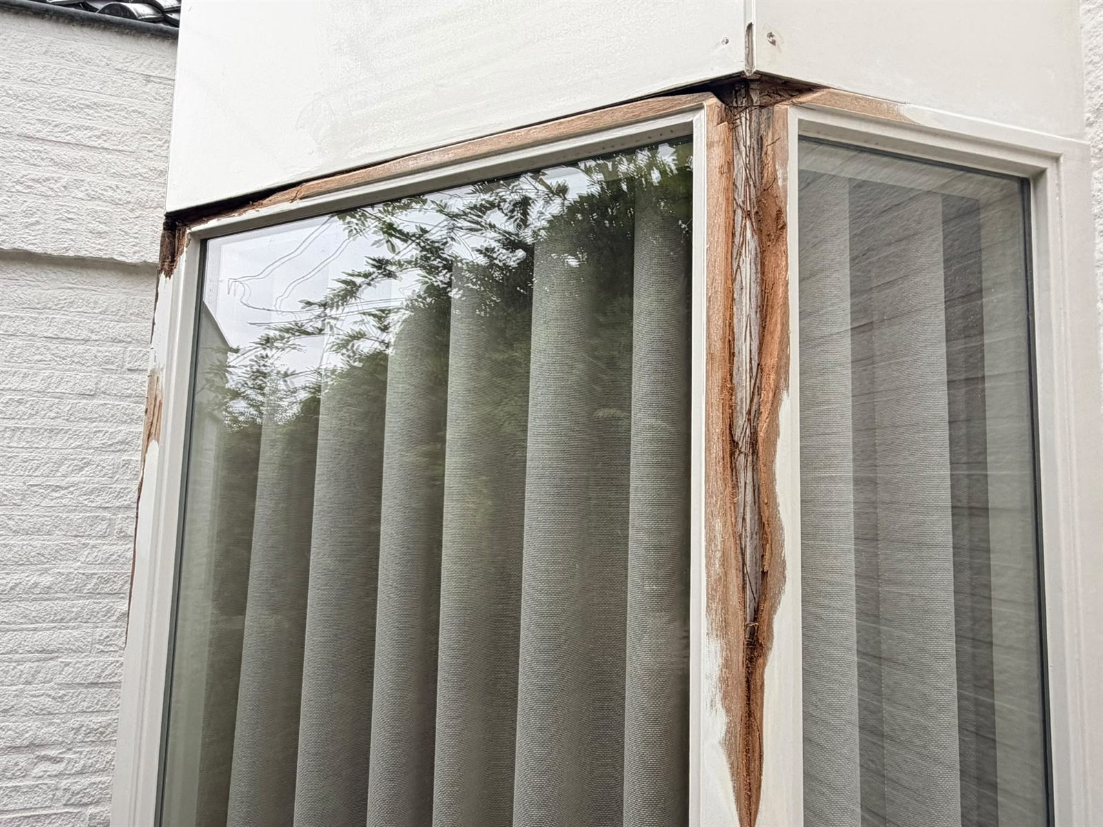 Hoekstijl van een houten kozijn met de verf eraf, blank hout en een scheur in de naad